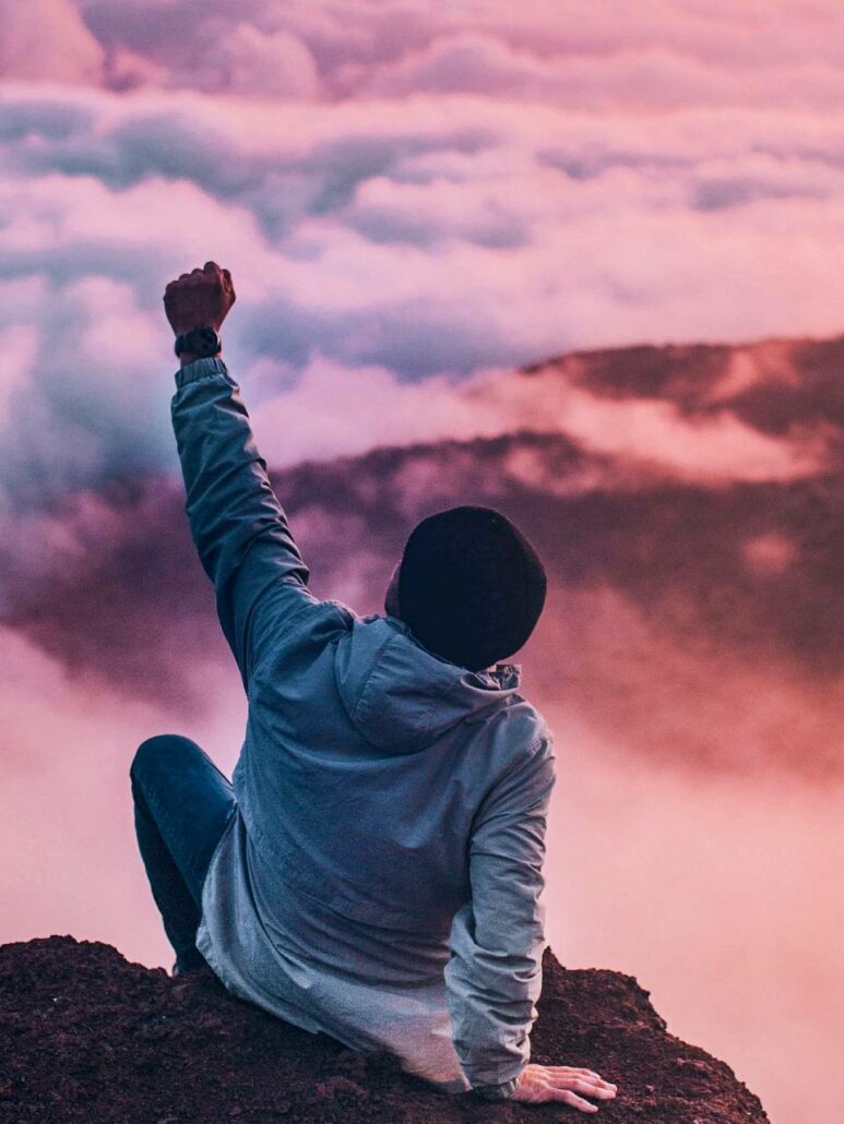 Person sitting on a mountain, fist in the air