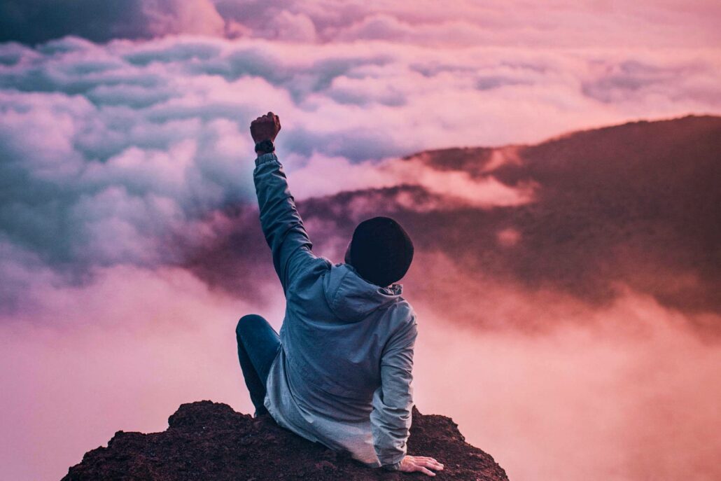 Person sitting on a mountain, fist in the air