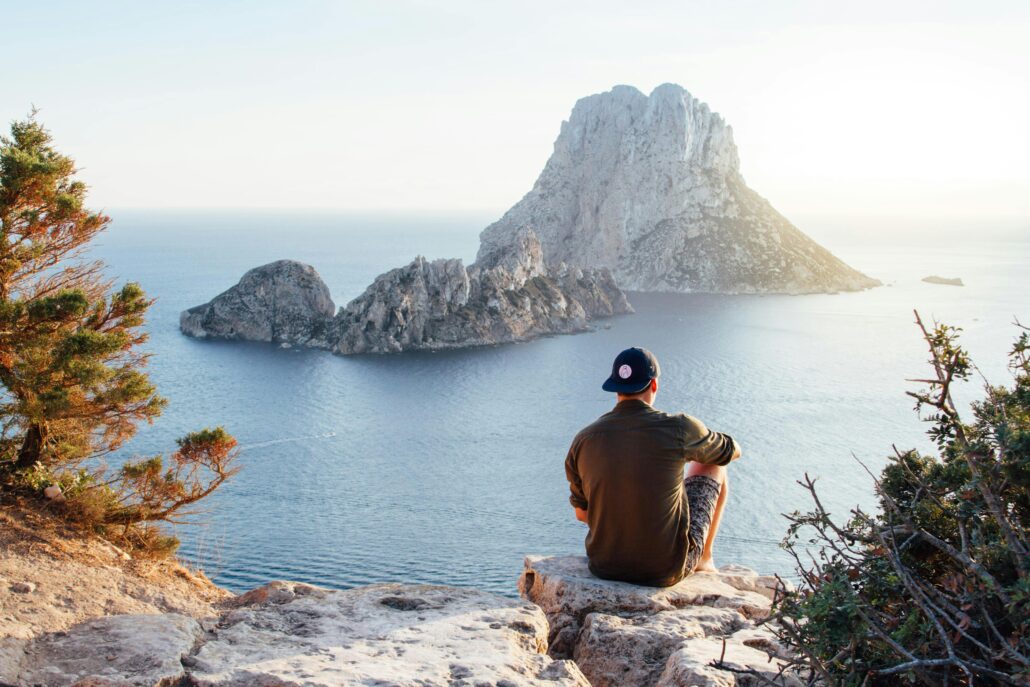 Man sitting on cliff, looking at sea.